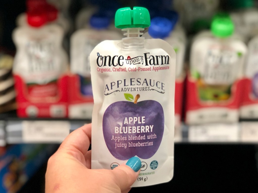 hand holding applesauce pouch in front of store shelves