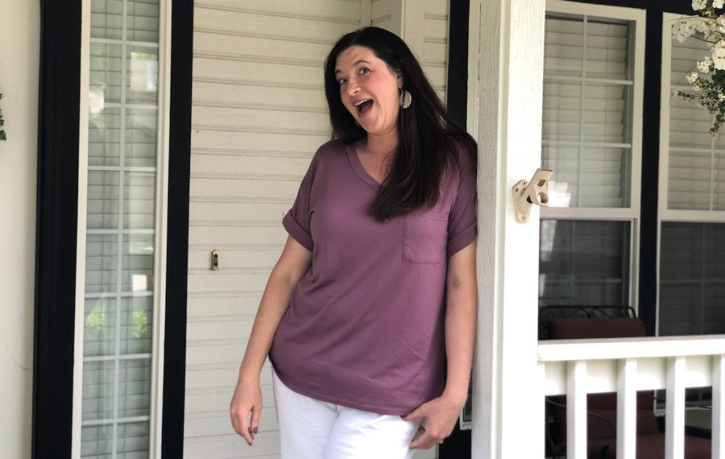 woman wearing purple short sleeve shirt and white pants standing outside on porch