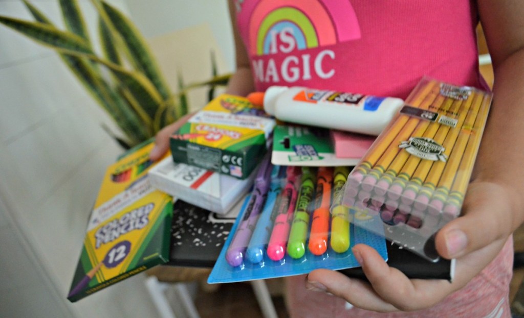 girl holding various school supplies writing utensils