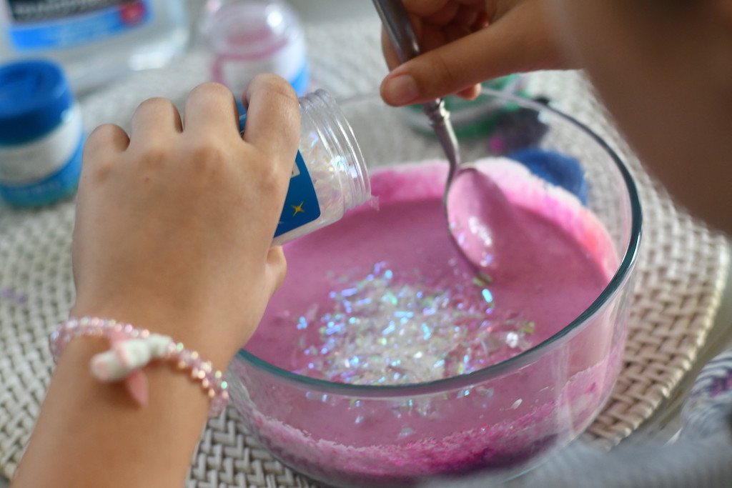 sprinkling glitter flakes into pink slime 