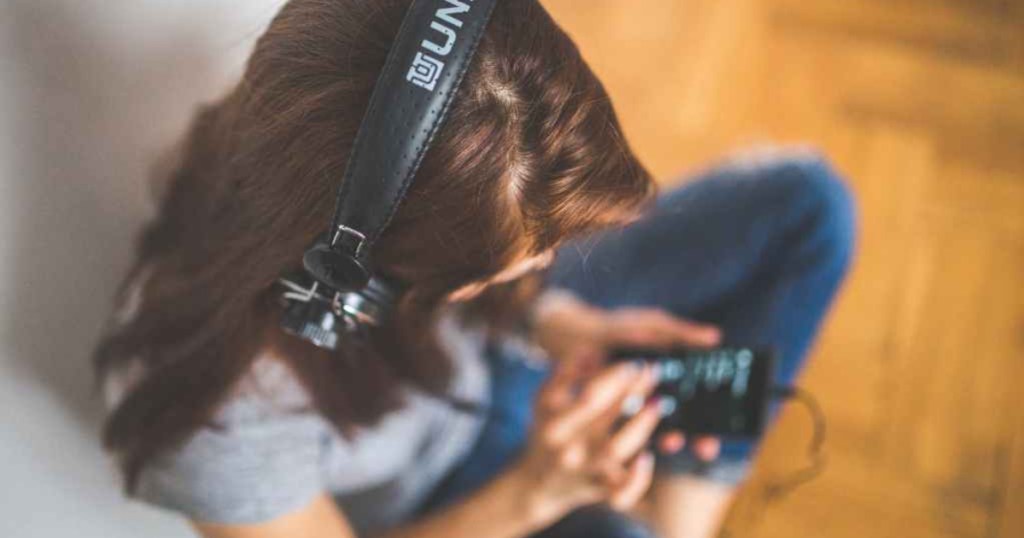 woman sitting on floor wearing headphones and holding a cell phone