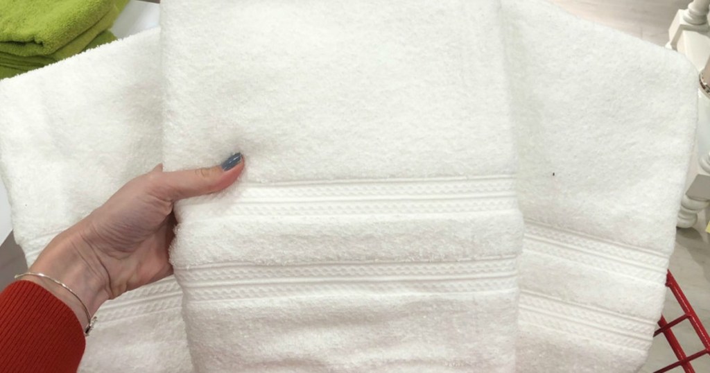 hand holding up home expressions white bath towels from cart