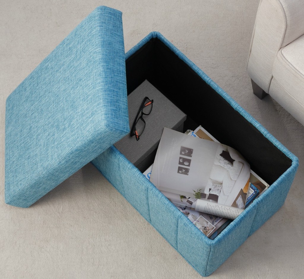 Blue denim fabric storage ottoman with papers and glasses being stored
