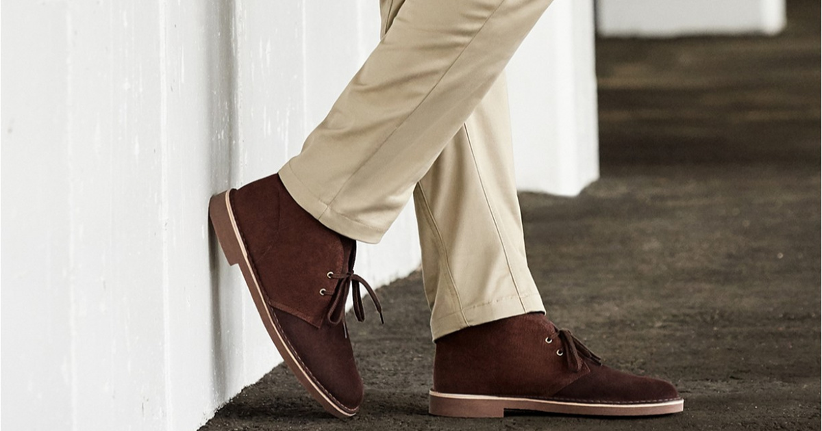 close up of man's feet wearing brown chukka boots leaning against wall