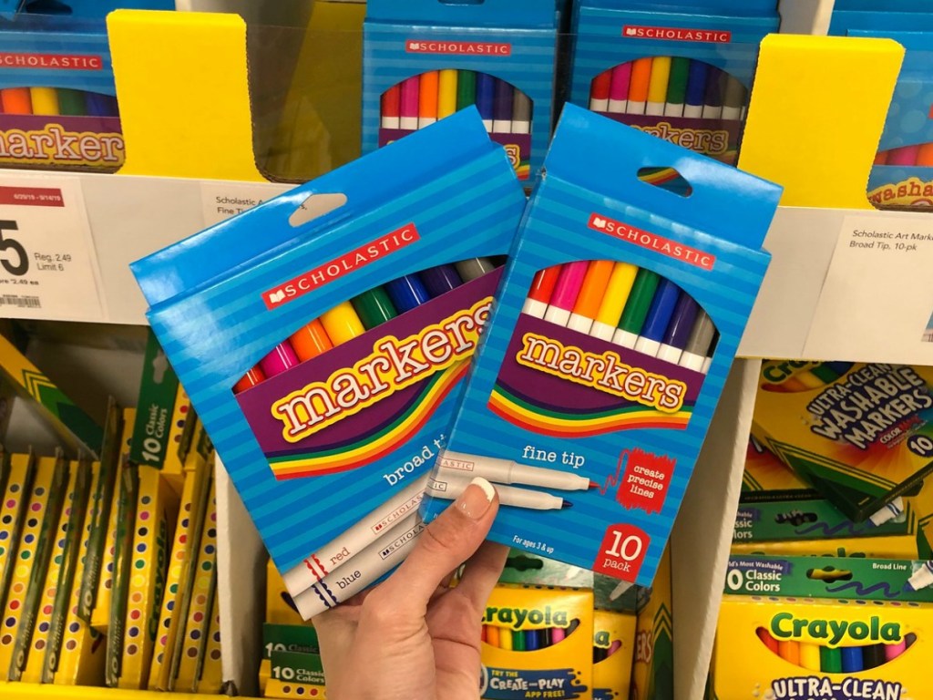 Hand holding two packs of Scholastic markers