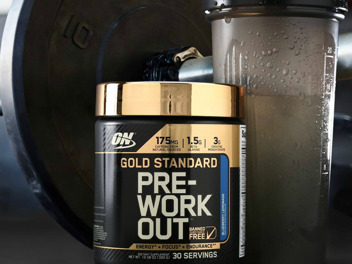 Optimum Nutrition Gold Standard Pre-Workout Powder in Blueberry Lemonade with shaker bottle and weights in background