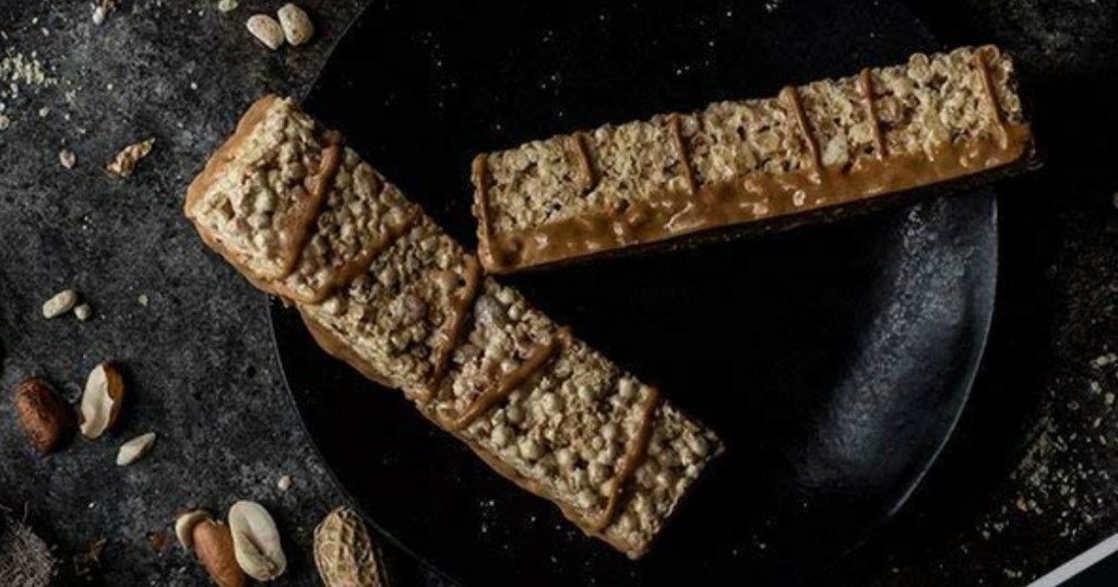 Two whole peanut butter protein bars on dark surface with peanuts