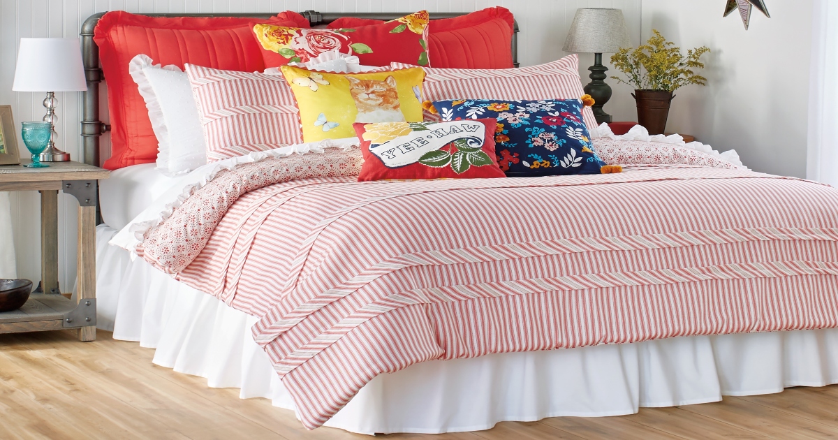 Pioneer Woman Striped red comforter on a fully made up large size bed with many decorative throw pillows.