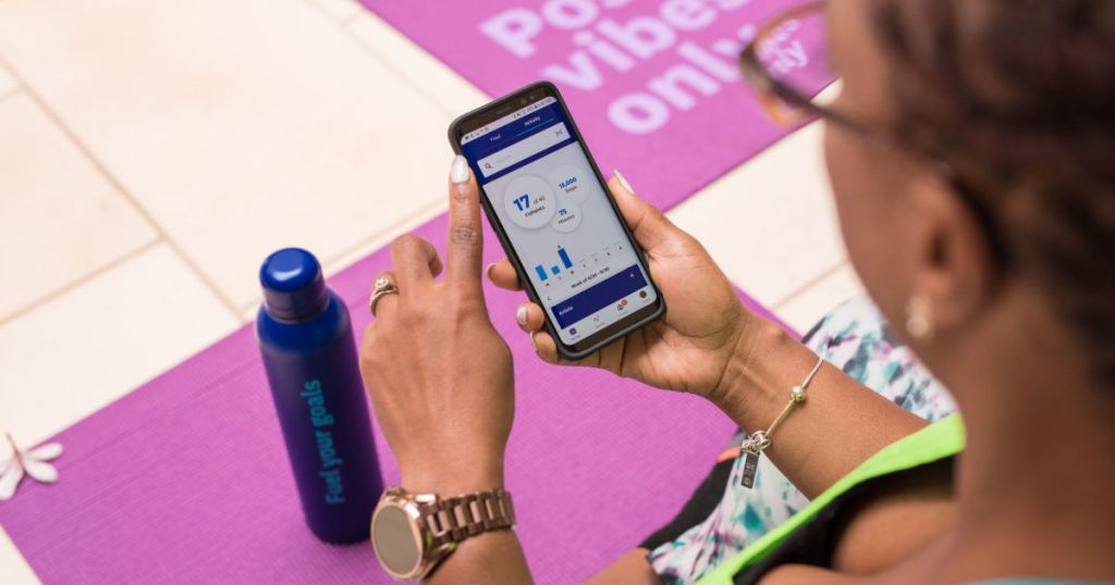 woman holding phone with Weight Watchers app and yoga mat