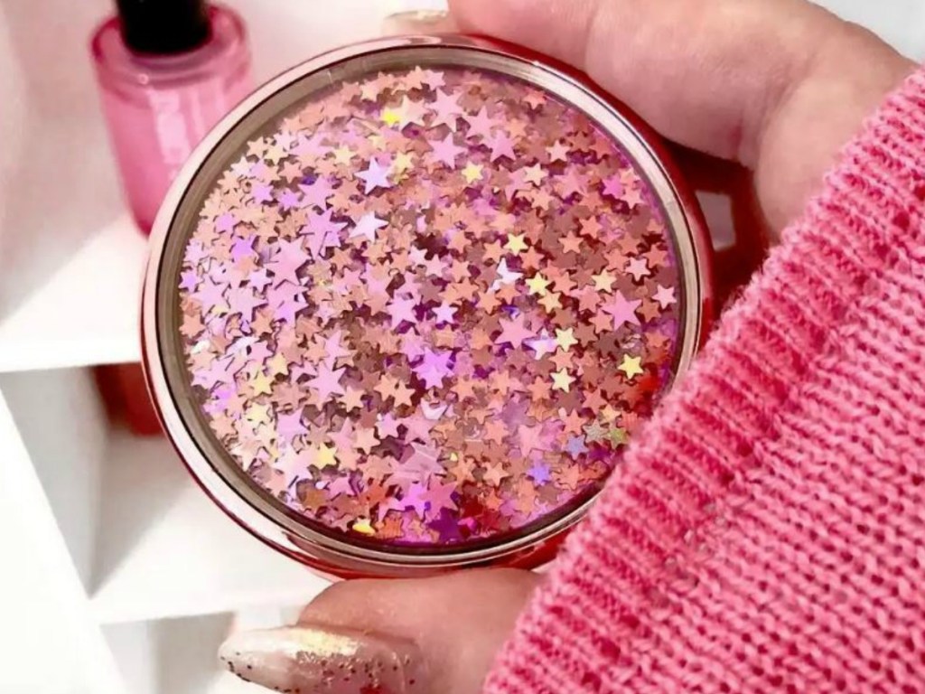 hand with pink sweater holding round pink make up 
