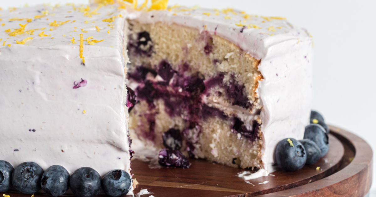 closeup of the baked, frosted, blueberry lemon cake with a slice out of it
