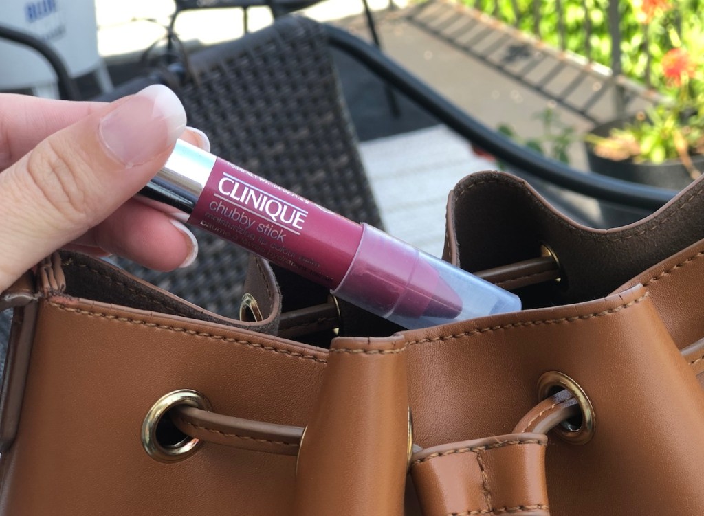 hand pulling pink lip balm out of brown leather bag