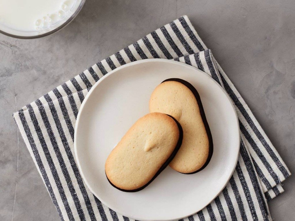 2 cookies on a plate with milk and a striped napkin