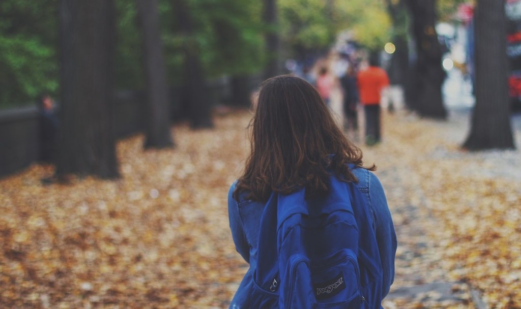 girl with blue backpack walking down leave covered street