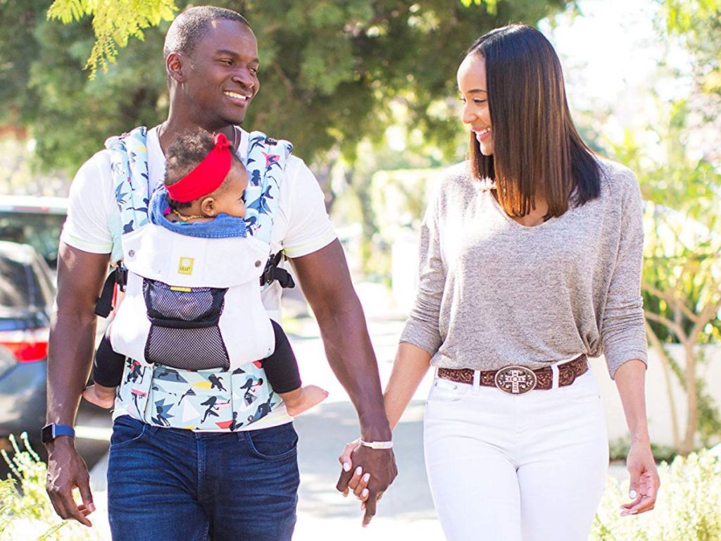 mom and dad walking with dad holding baby in lillebaby incredibles 2 disney carrier