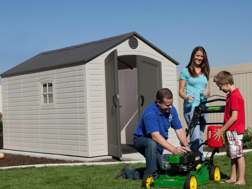 family starting lawn mower outside by shed
