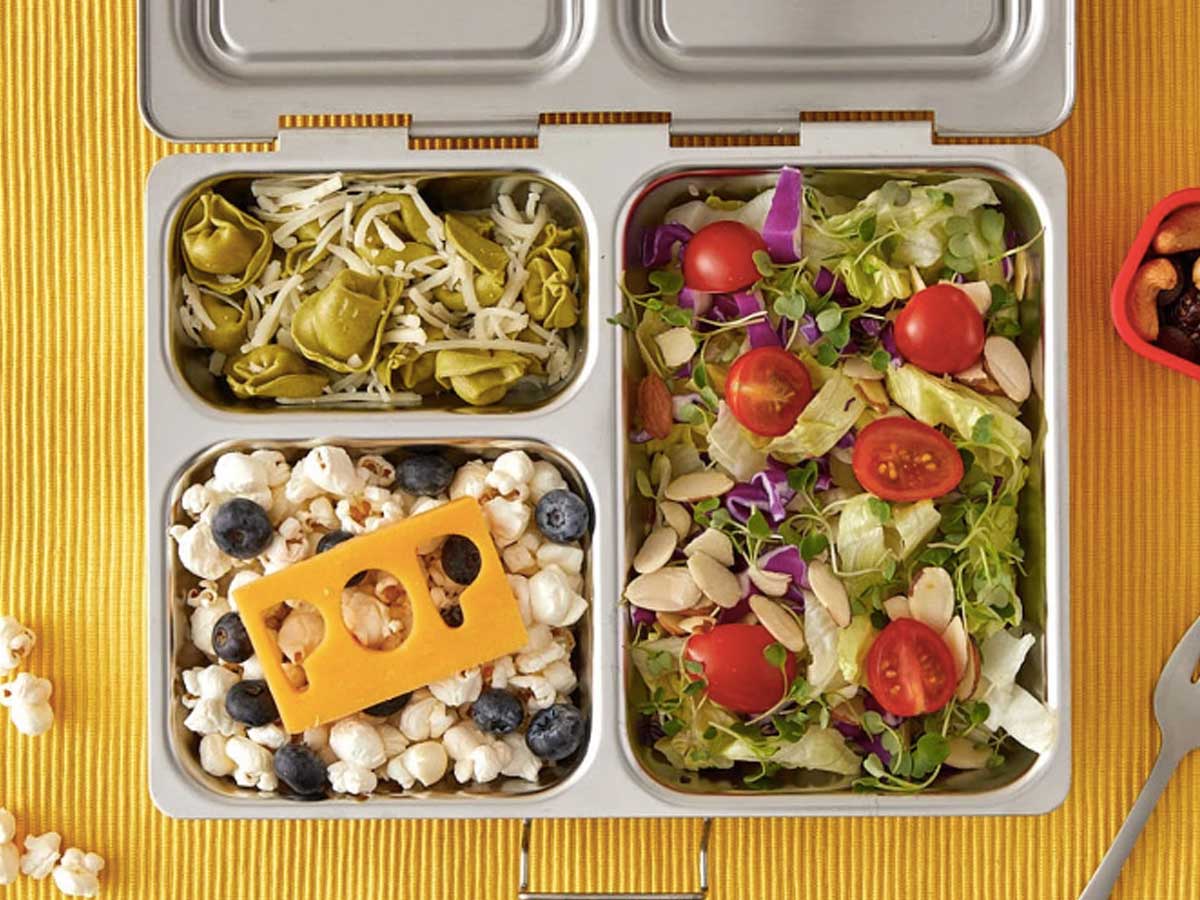 metal lunchbox with pasta, salad, fruit and popcorn filling three compartments