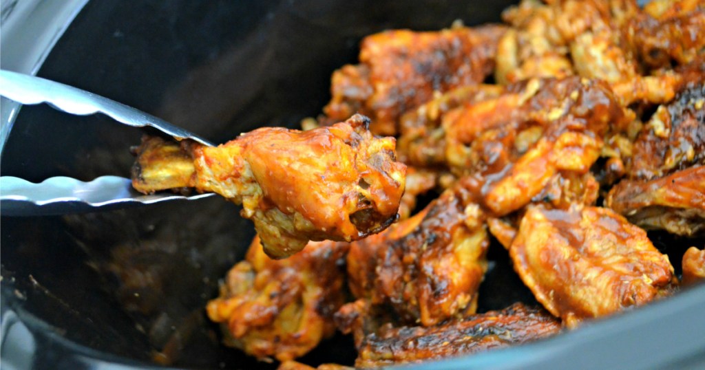 pulling out chicken wing from crock-pot slow cooker