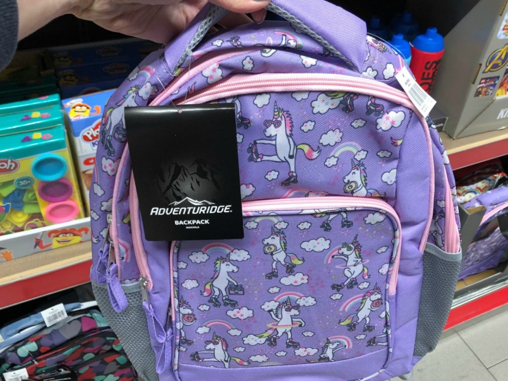 hand holding purple backpack with unicorns by store display