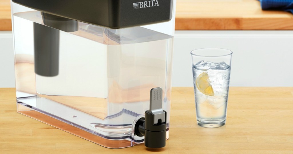 Brita water filter with black lid on counter filled near cup with lemon water