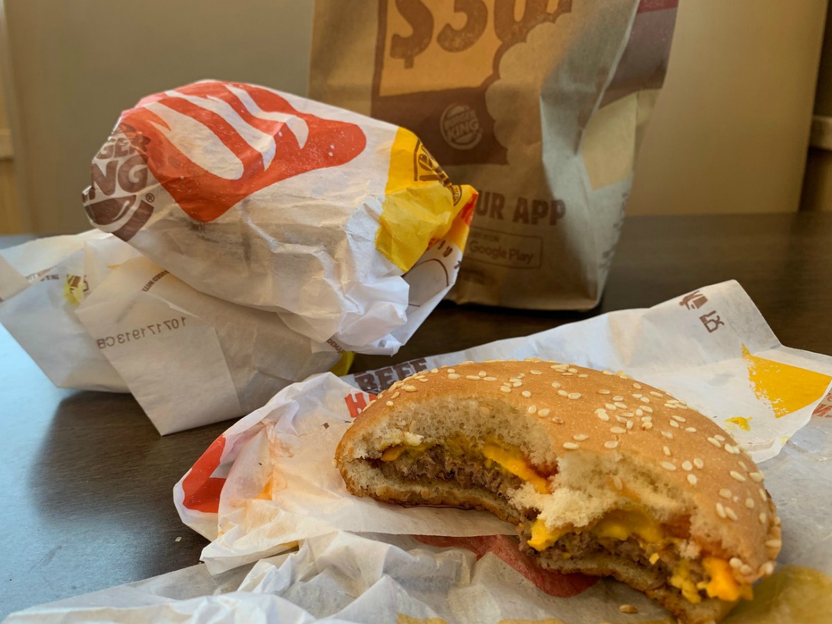 half-eaten Burger King Cheeseburger next to wrapped cheeseburgers and bag