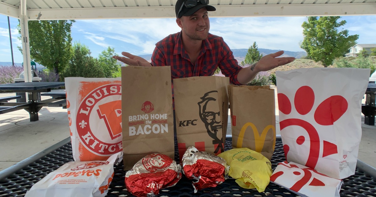 man at table with 5 different chicken sandwiches from fast food restaurants