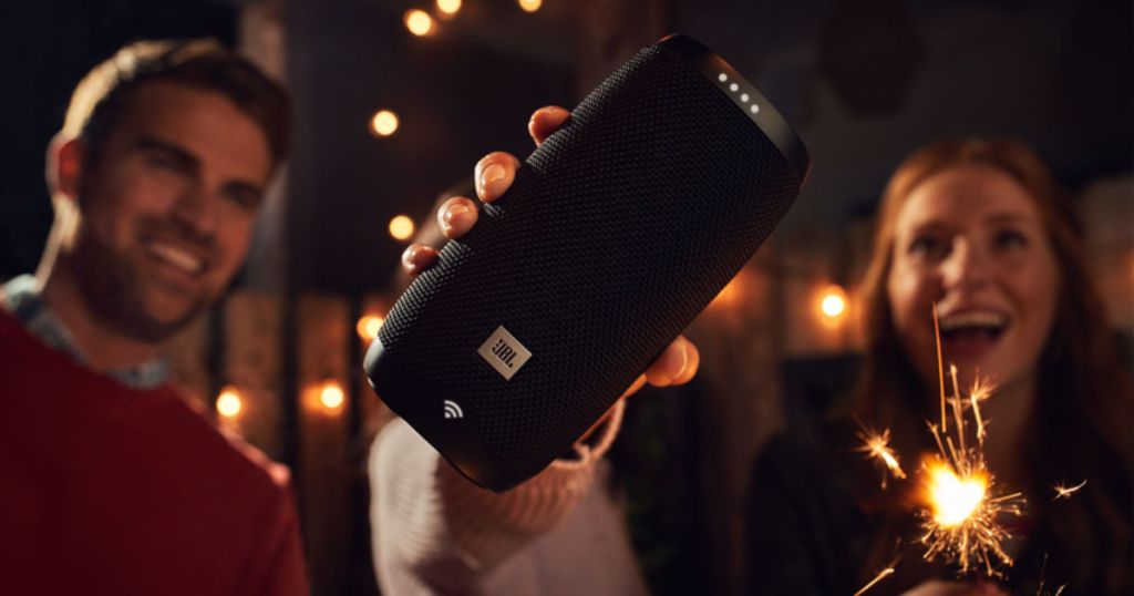 hand holding JBL LINK 10 Portable Bluetooth Speaker with people in the background and sparklers