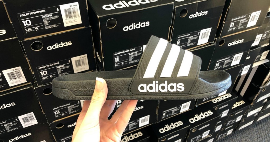 woman holding adidas slides in front of adidas shoe boxes