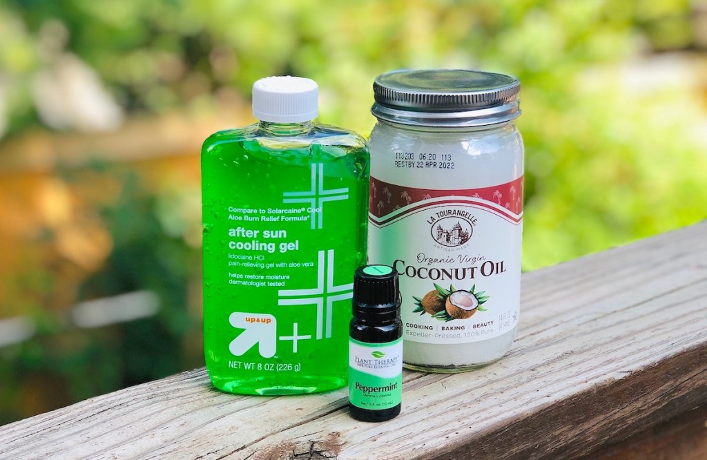 bottle of green aloe vera gel jar of coconut oil and peppermint essential oils on wood railing outside 