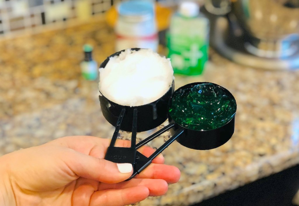 hand holding two black measuring cups with white and green gels