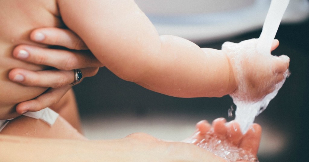 baby holding hand under running water while woman holds him