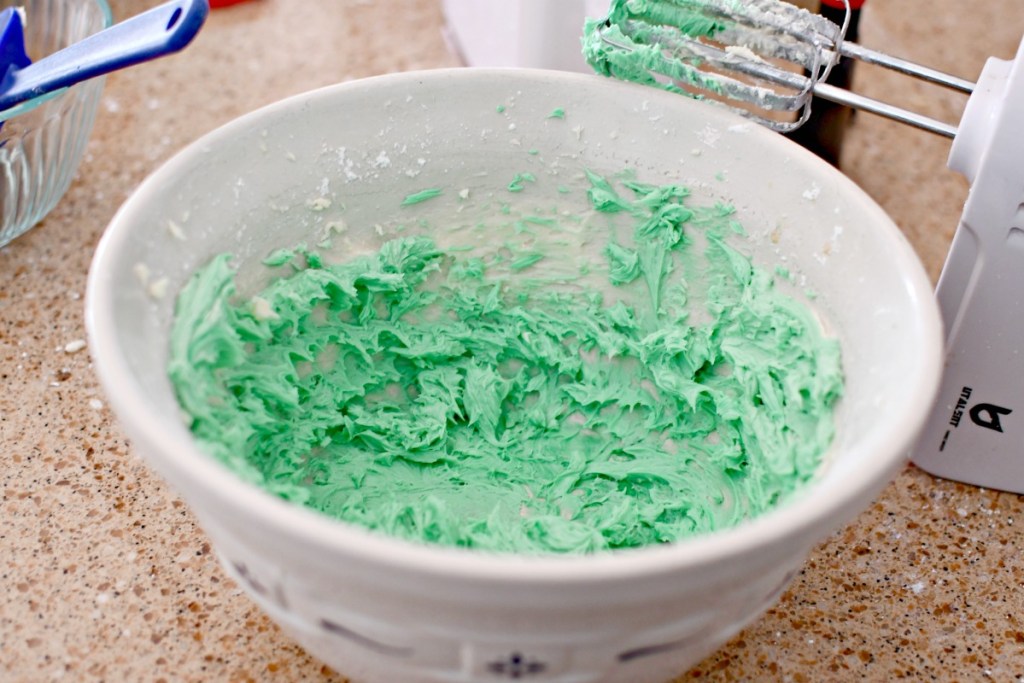 mixing buttercream frosting with green food coloring