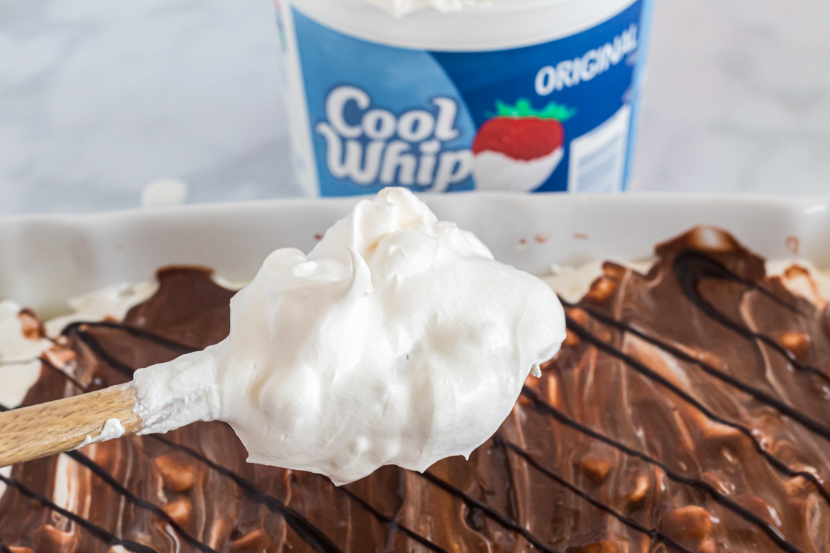 adding cool whip to the top of smores lasagna with spoon