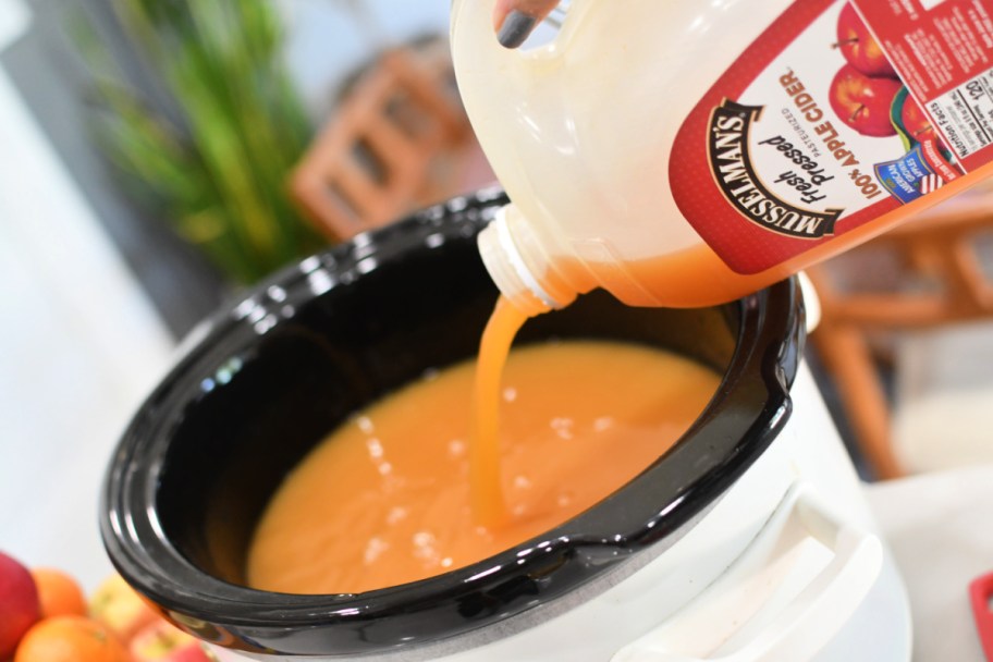 pouring apple cider into a slow cooker