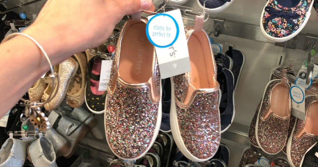 Pink glittery slip on shoes for toddler girls on hanger in hand in-store