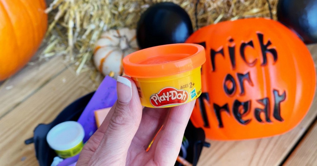 woman holding Halloween Play-Doh mini can next to Halloween decor