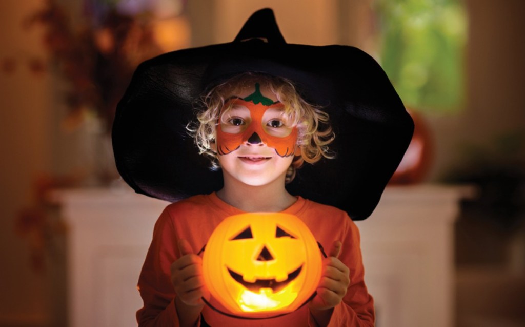 boy wearing witch costume holding pumpkin