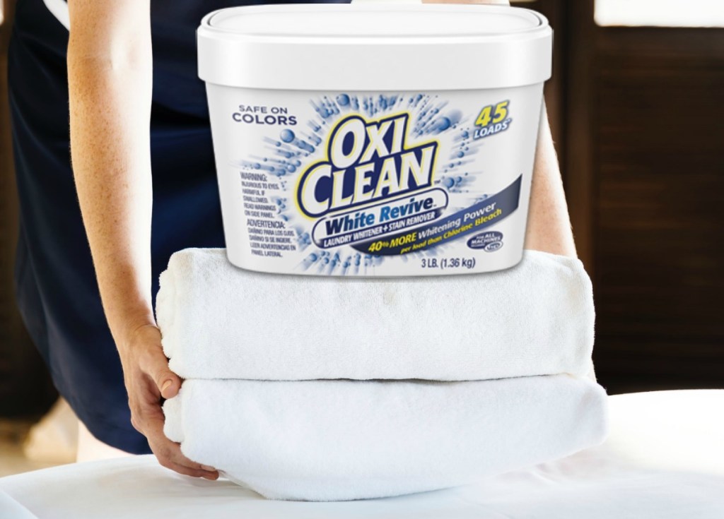 Woman stacking two folded towels with a tub of OxiClean on top