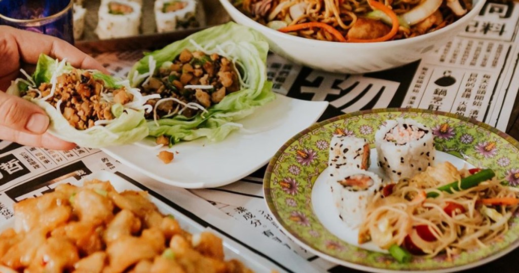 hand picking up wrap with Asian food on table