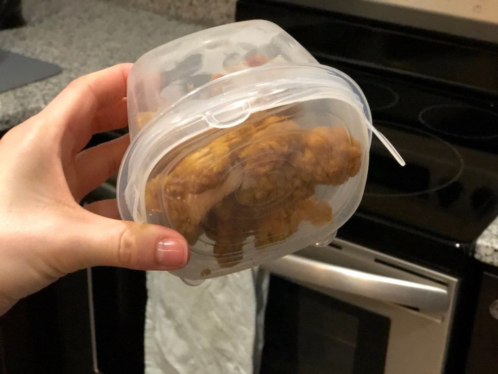 holding tupperware container with leftovers inside and silicone stretch lid on top