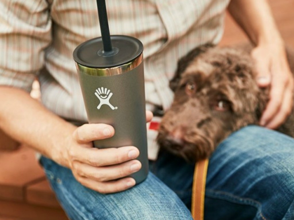 man holding cup with straw and dog on his lap