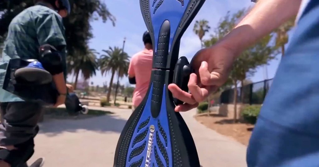 boy holding a blue razor ripstick in the park with kids around