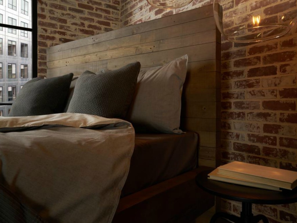 bed with blankets & sheets next to brick wall