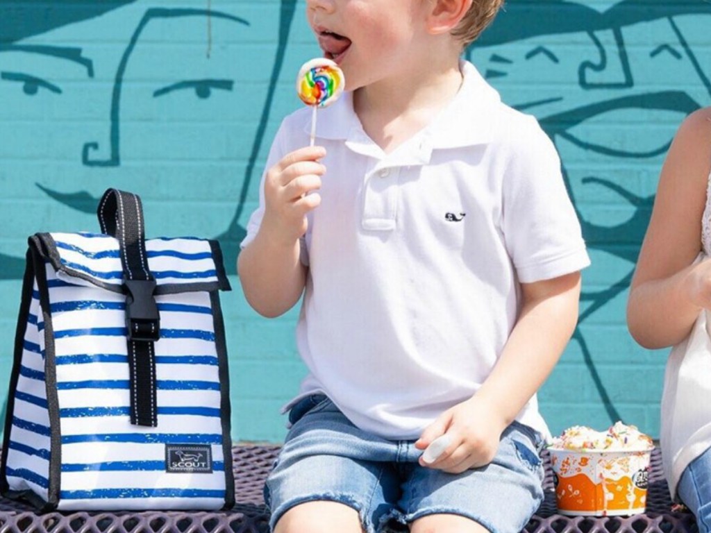 child licking sucker sitting on bench