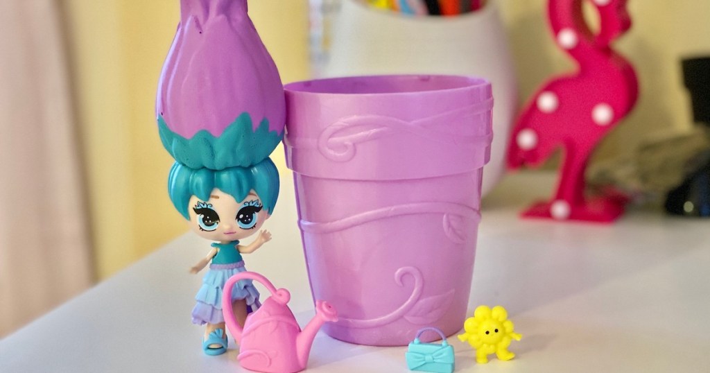 purple and blue doll standing on desk next to flower pot toy and accessories