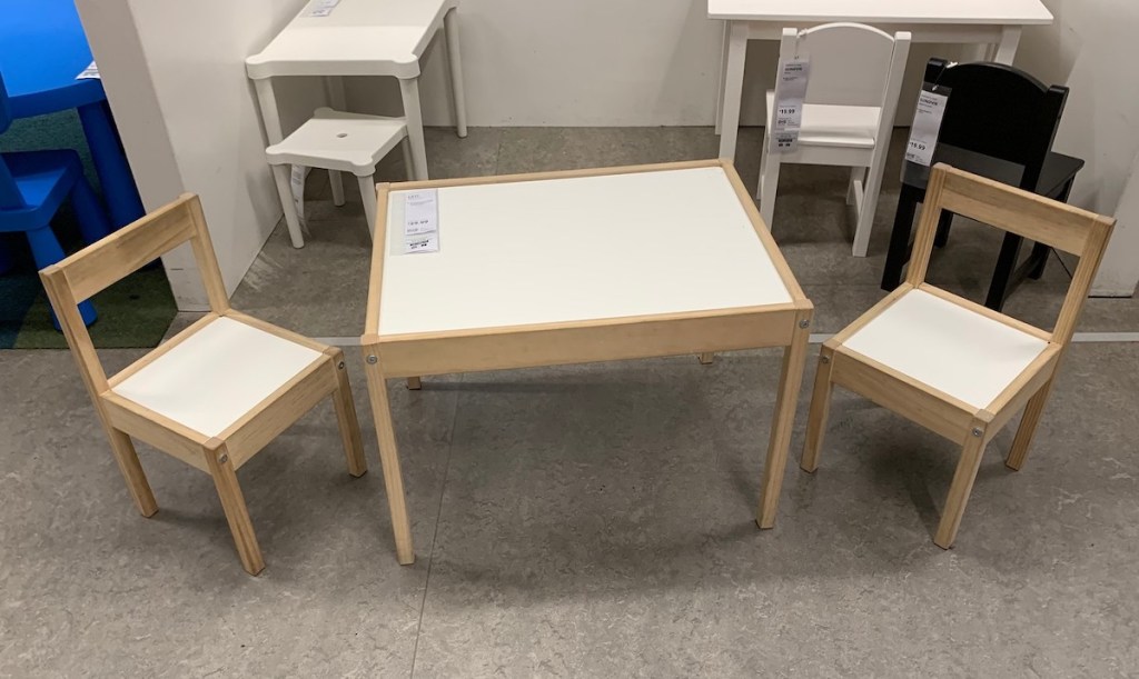 white and natural wood colored table and two chairs sitting on cement floor 