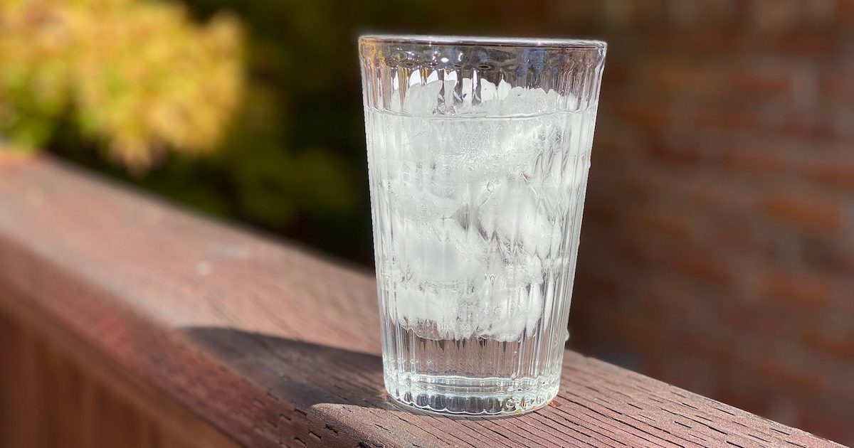 glass of ice water sitting outside on brown deck 