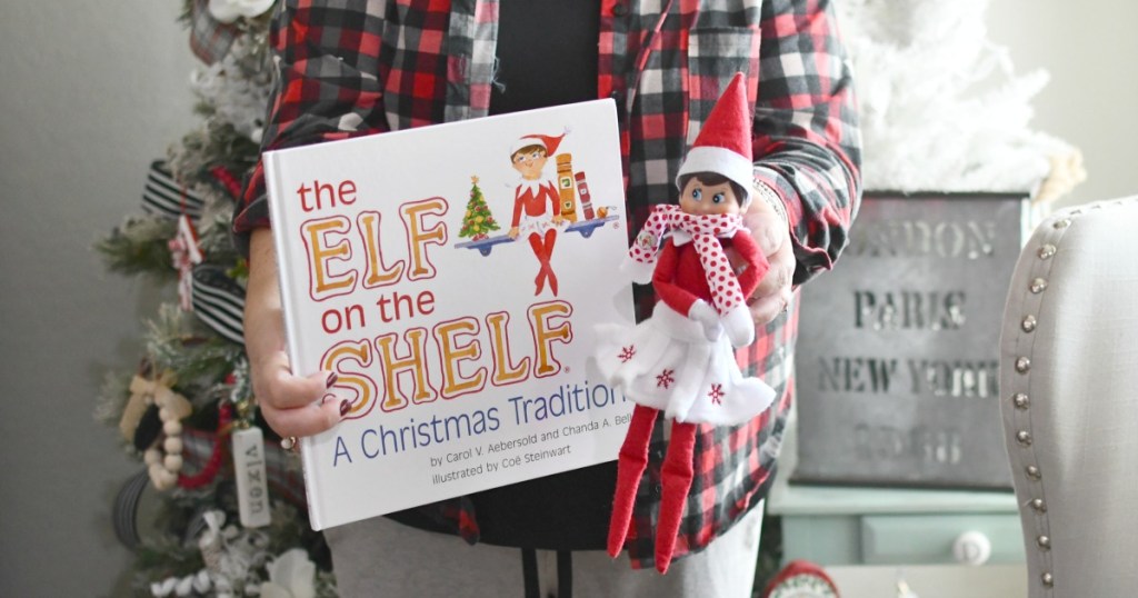 holding an elf on the shelf by the tree