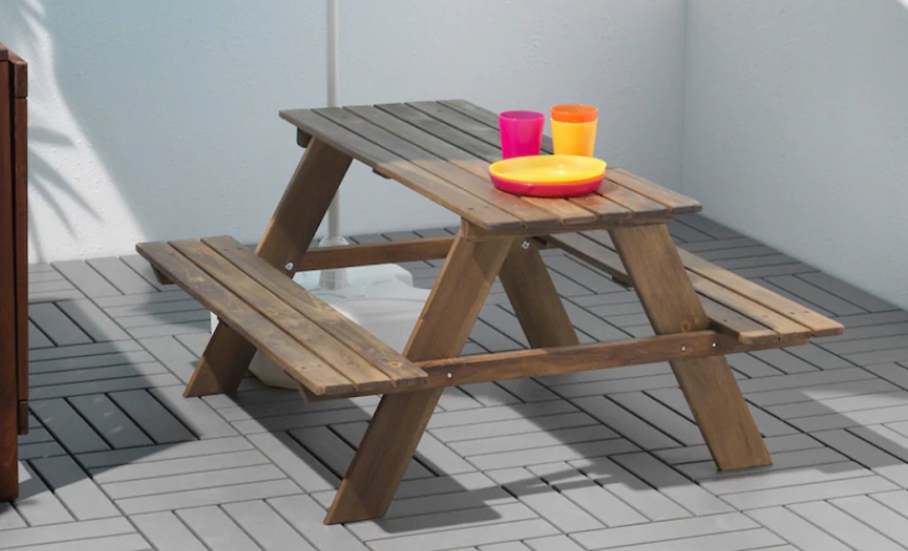 brown wood picnic table with bright colored dishes on top 