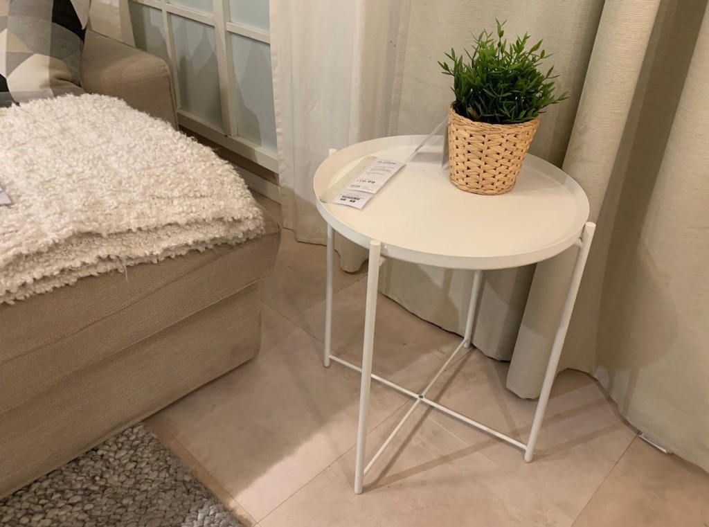 white tray table with small green plant on top next to bed 